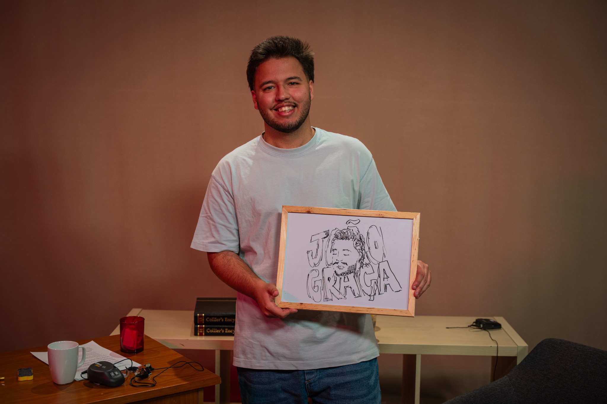 Um participante no cenário do Ângulo segura uma ilustração emoldurada.
