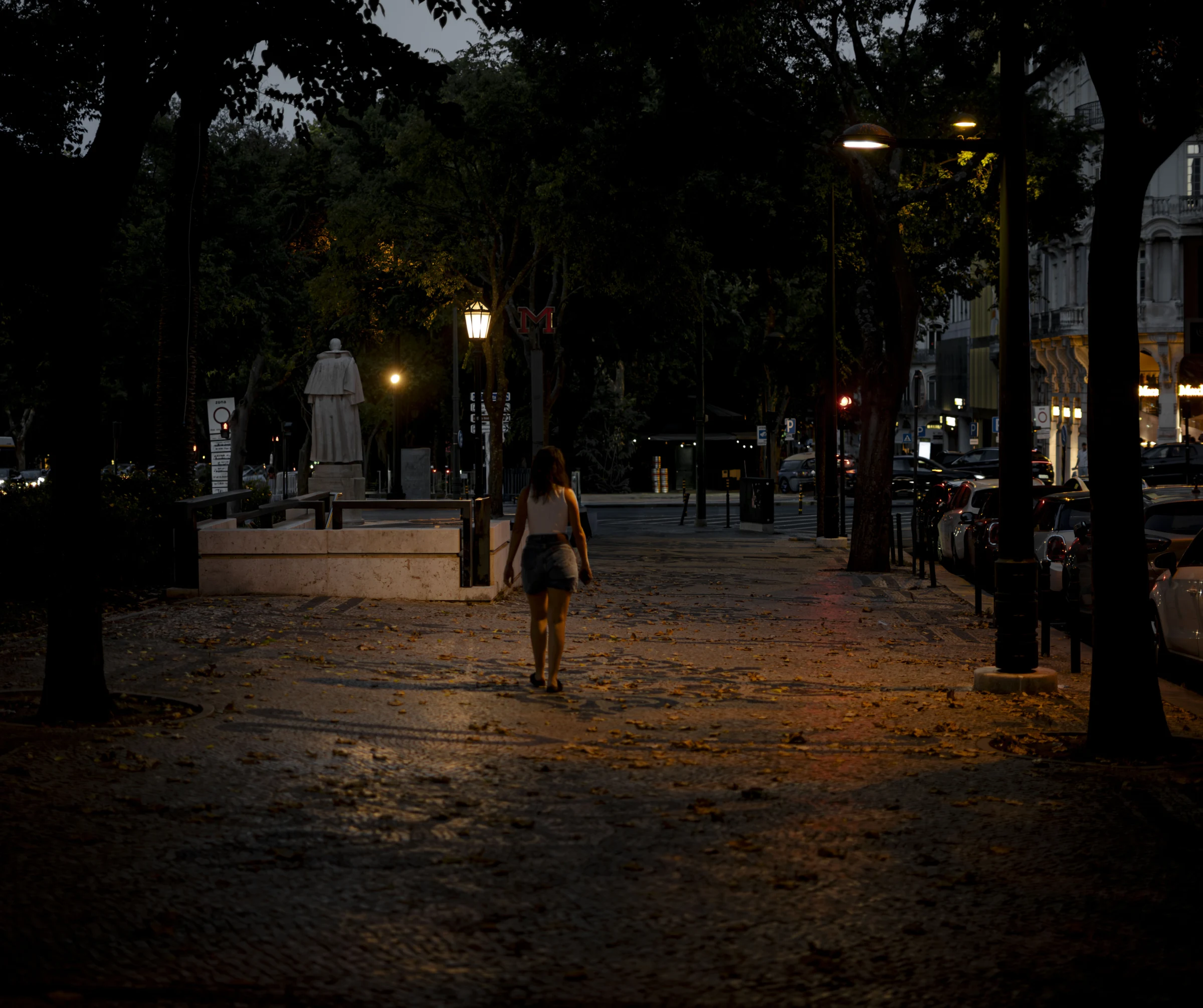 Uma pessoa atravessa a praça de Lisboa à noite.
