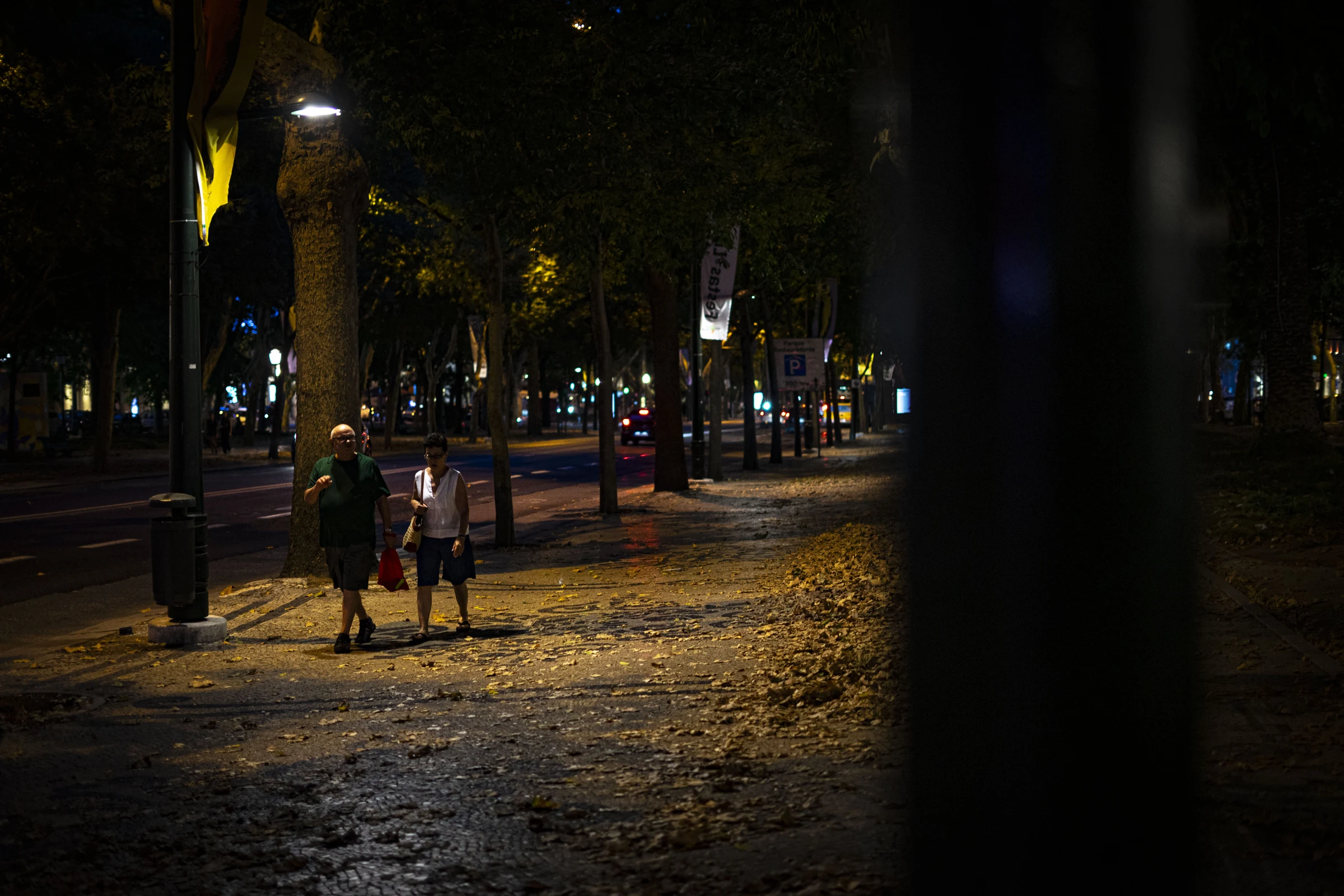 Pessoas atravessam uma praça à noite.